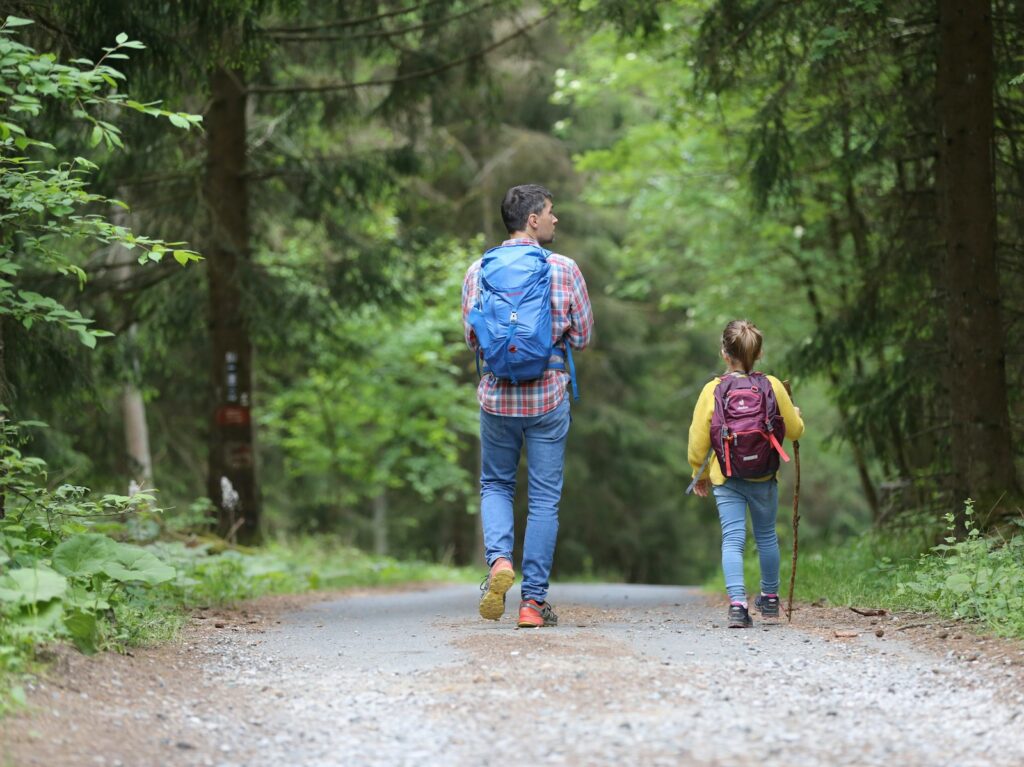 a man and girl walking on a trail with backpacks