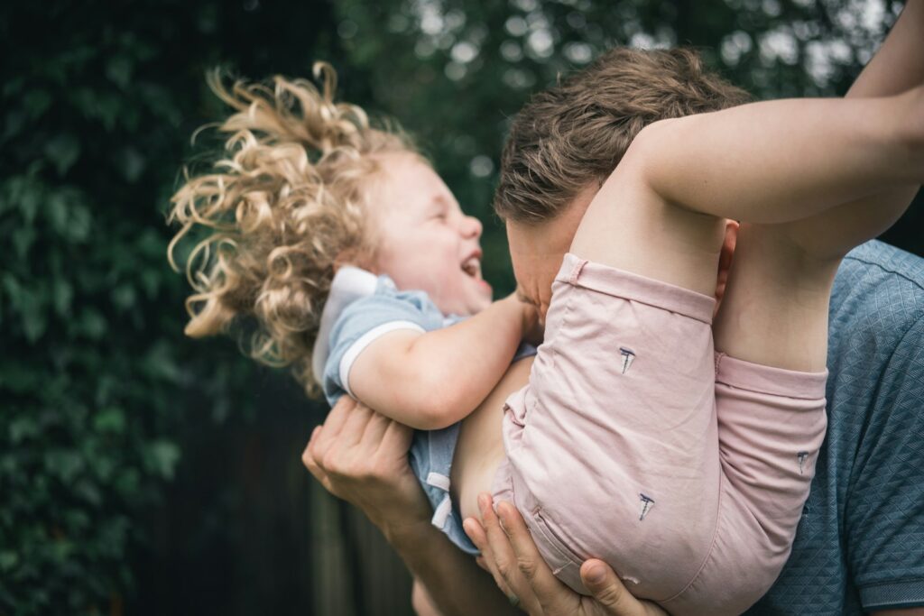 woman in pink sleeveless dress carrying baby in white shirt from article 5 Mindful Ways Dads Can Support a Child’s Anxiety